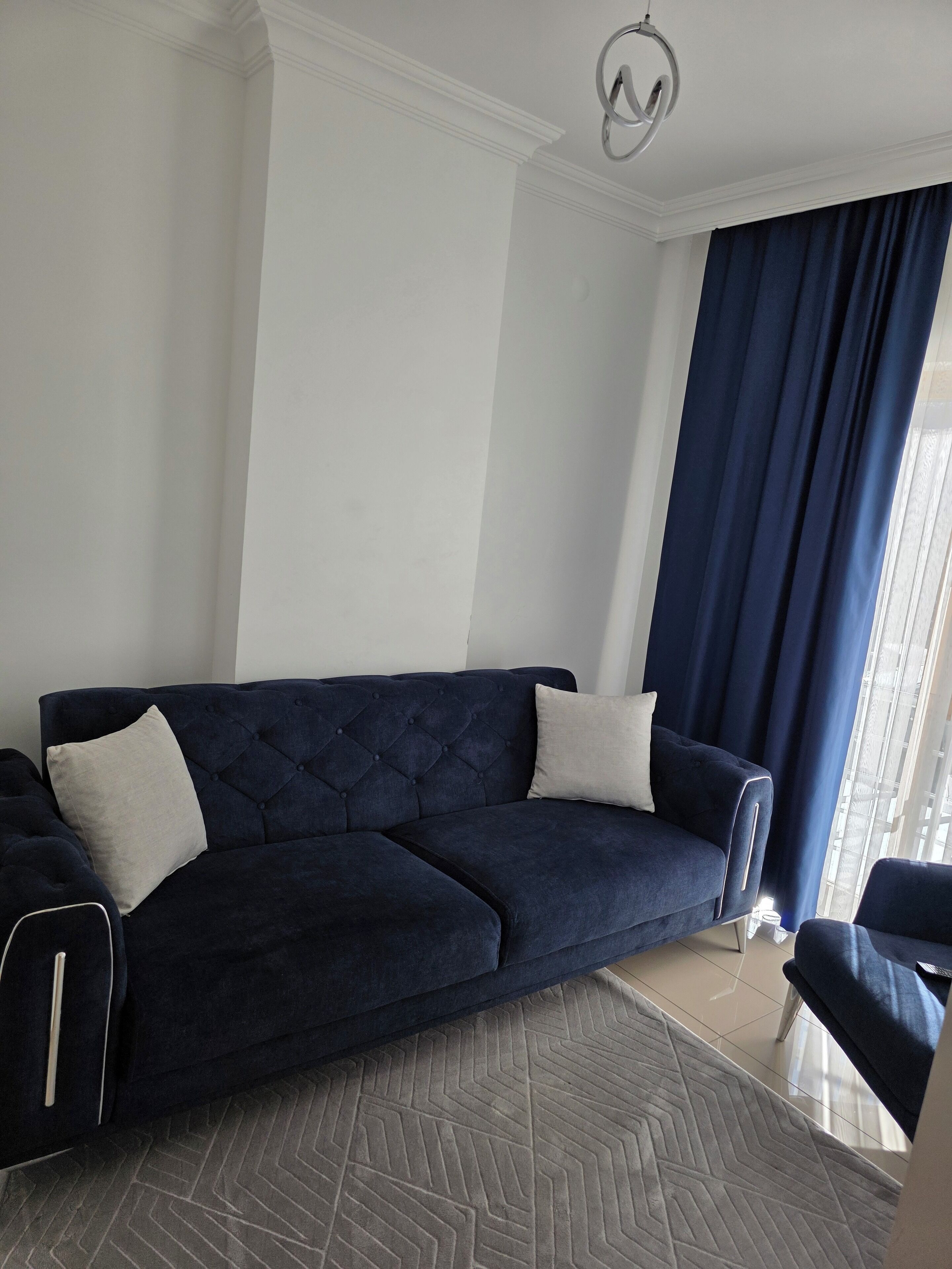 Un sofá azul oscuro con cojines blancos en una habitación con paredes blancas y un tapiz de diseño en espiga.