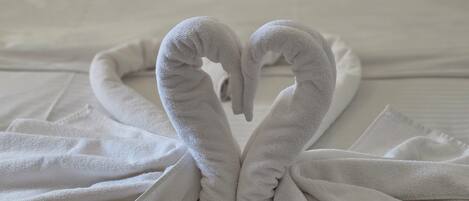 Cama bem arrumada com lençóis brancos e arranjo de toalhas em formato de coração na cama.