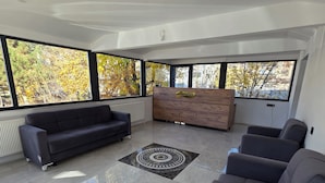 Amplia sala de estar con un sofá oscuro, un mostrador de recepción de madera y ventanas grandes que ofrecen vistas a árboles.