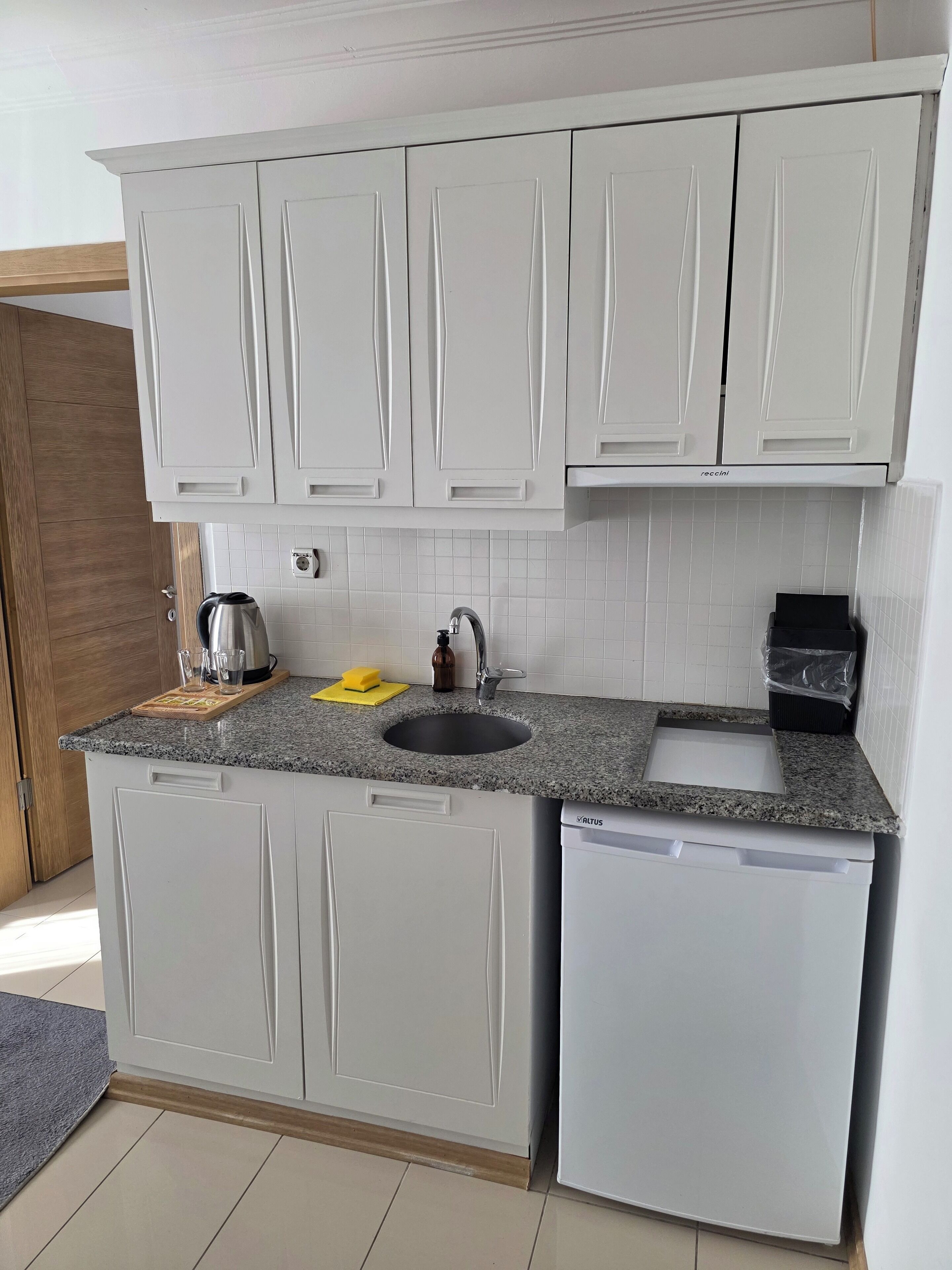 A compact kitchen with white cabinets, a granite countertop, a built-in dishwasher, and a small sink.