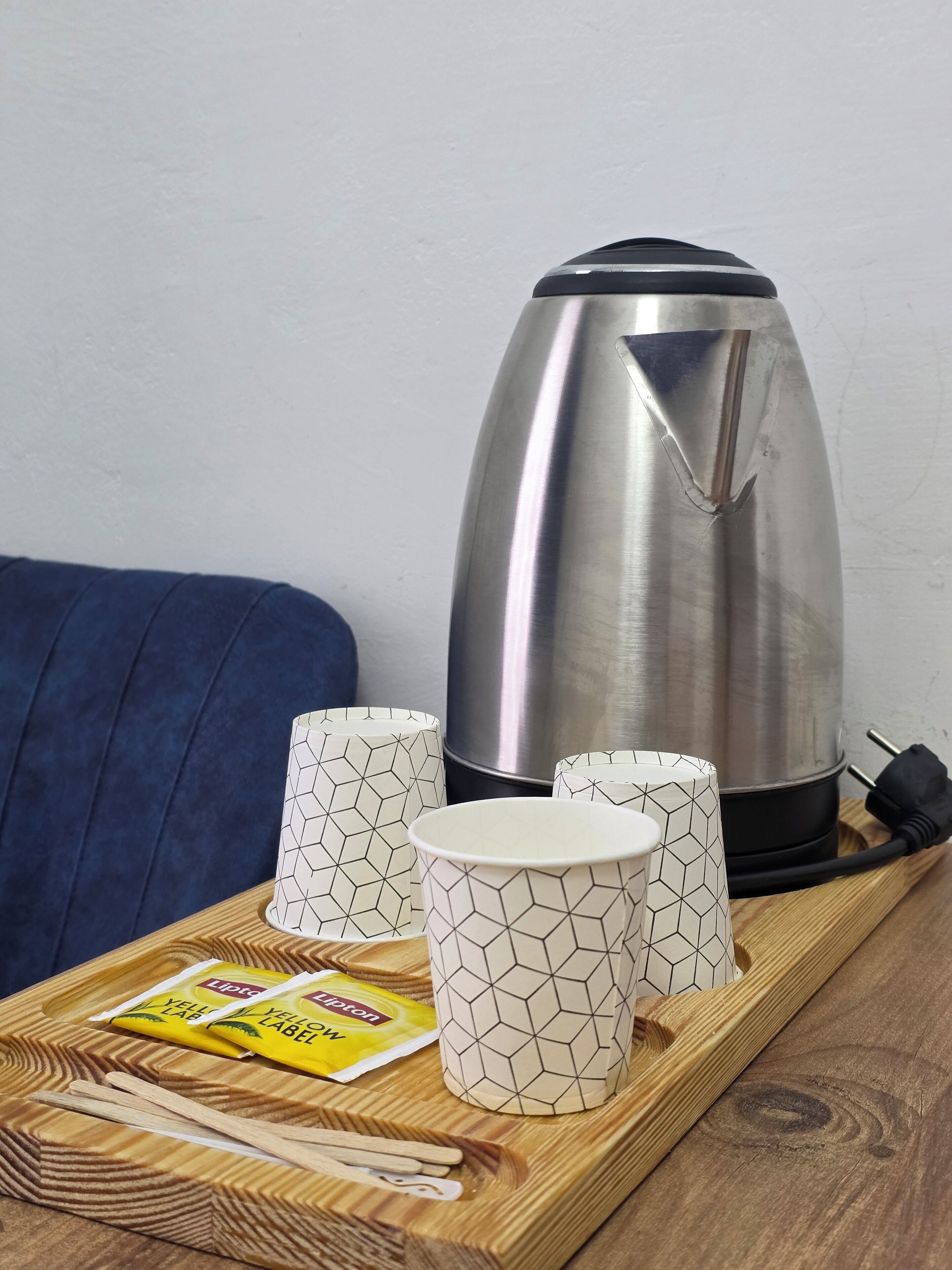 A stainless steel kettle, four patterned cups, a yellow packet, and wooden chopsticks on a tray.