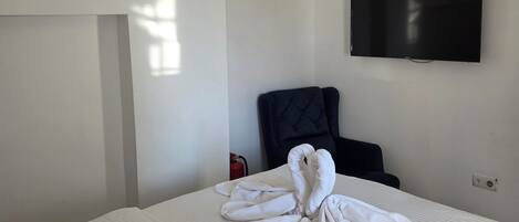 A hotel room with a neatly made bed, a flat-screen TV mounted on the wall, a black upholstered chair, and a ceiling light fixture.