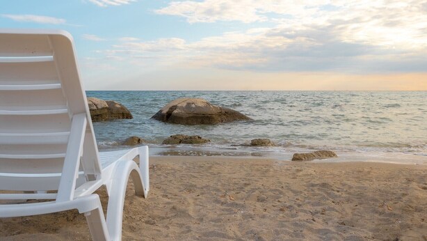 A beach with a white plastic chair and large rocks in the water. - Modern semi-detached house, quiet location, 6 minutes to the coast. (Bašanija)
