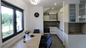 A modern kitchen with white cabinets, a dining area with a wooden table and blue chairs, and a large window with a view of greenery. - Modern semi-detached house, quiet location, 6 minutes to the coast. (Bašanija)