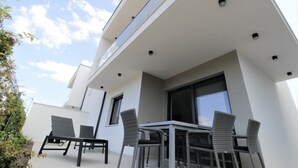 A modern outdoor patio with a table and chairs, a large window, and a white building facade. - Modern semi-detached house, quiet location, 6 minutes to the coast. (Bašanija)