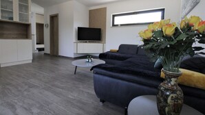 A modern living room with a sofa, a coffee table, and a TV. There is a vase with flowers on a side table. - Modern semi-detached house, quiet location, 6 minutes to the coast. (Bašanija)