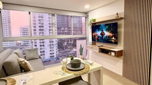 Un salon moderne comprenant un coin repas, de grandes fenêtres, un téléviseur à écran plat et une vue sur la ville.
