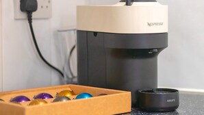 A Nespresso coffee machine with a Krups brand coffee pot, a box of coffee capsules, and a power cord plugged into a wall socket. - 5 Bedroom Premium Apartment Central London (London)
