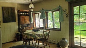 Un comedor con una mesa dispuesta para cuatro, sillas de madera, una araña y un ventanal con cortinas.