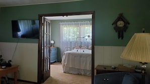 Un dormitorio con una cama, televisión montada en la pared, un reloj y una ventana con cortinas.