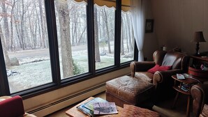 Una habitación acogedora con un sillón de cuero, una mesita de madera con revistas, y vistas a un paisaje nevado a través de grandes ventanales.