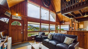 Ein geräumiges Wohnzimmer mit einer Ledersofa, Holzwänden, großen Fenstern und Blick ins Freie.