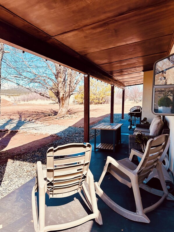 A covered patio area with two rocking chairs, a table, and a chair.