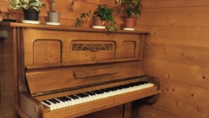 A wooden piano with a bench, surrounded by potted plants on a wooden shelf. - Chalet le muveran, in the center of gryon with garden! (Gryon)