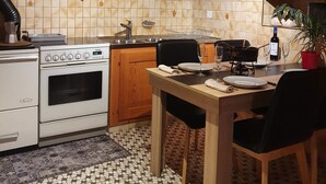 A kitchen with wooden cabinets, a stove, a dining table with chairs, and a potted plant. - Chalet le muveran, in the center of gryon with garden! (Gryon)