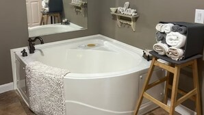 Un baño con una bañera grande, un taburete de madera con toallas y un espejo con un letrero que dice 'relájate'.