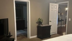 Un dormitorio con una cama, un aparador, un televisor, un ventilador de techo y una puerta que da a otra habitación.