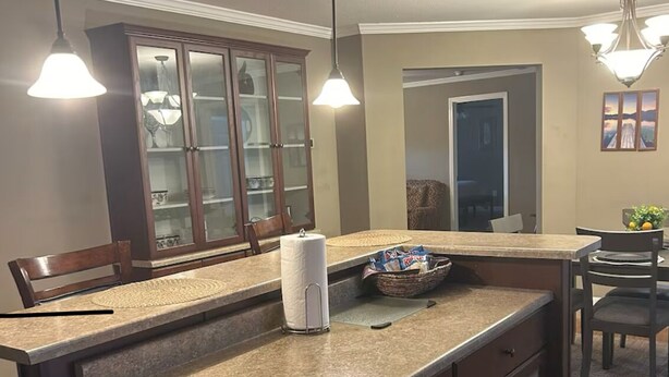 Una cocina con encimera de granito, armarios de madera y una isla integrada. Se observan luces colgantes, un refrigerador y una zona de comedor.