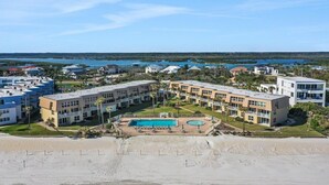 Un hotel frente a la playa con varias edificaciones, una piscina y vistas al océano y cuerpos de agua.