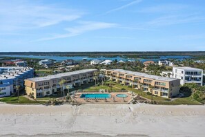 A beachfront hotel with multiple buildings, a swimming pool, and a view of the ocean and water bodies.
