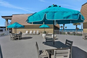 An outdoor seating area with tables and chairs, some with umbrellas, and a view of the ocean.