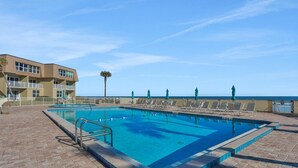Una piscina con vista despejada al océano, rodeada de sillones de descanso y un edificio con balcones.