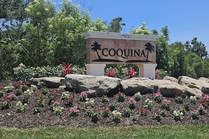 A sign with the name 'COQUINA' and the number '7900' in a landscaped area with rocks and flowers.
