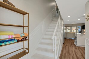 A staircase with white railings leading to a kitchen area with white cabinets and a wooden floor.
