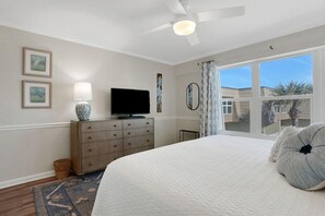 A bedroom with a bed, a dresser, a television, and a window with a view of buildings.