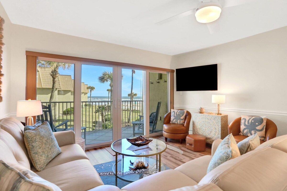 A living room with a sofa, armchairs, a coffee table, and a TV mounted on the wall.