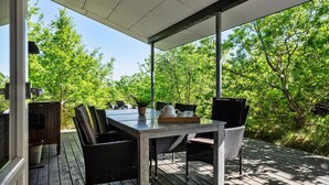 Eine Terrasse im Freien mit Tisch und Stühlen, umgeben von üppigem Grün.