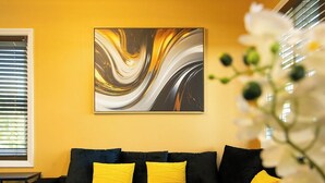 A living room with a black sofa, yellow cushions, and a large abstract painting on the wall.