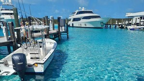 A marina with clear blue water, boats docked, and a large yacht in the background.