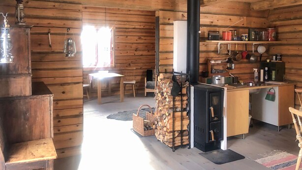 L’intérieur chaleureux d’un chalet avec un coin repas en bois, une cuisine équipée d’une cuisinière et une cheminée.