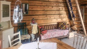 L’intérieur d’un chalet accueillant, avec un plancher en bois, un banc en bois, une table avec une bougie, une lanterne et une échelle.