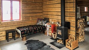 Une pièce chaleureuse dans un chalet en rondins, avec un lit, un poêle à bois, une fenêtre et une cheminée.