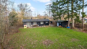 A cabin with a fenced yard, a small shed, and a tree in the foreground. - Stunning home in Holbæk with sauna (Holbæk)