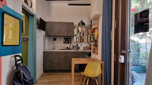 Una cocina compacta con electrodomésticos modernos, un comedor con mesa de madera y sillas amarillas, y vistas al exterior a través de un ventanal.