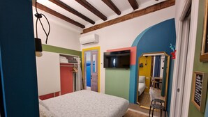Un dormitorio con cama, armario, televisión y baño visible a través de un arco.