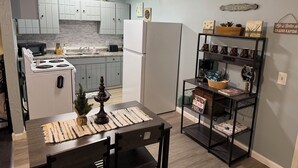 A modern kitchen with white cabinets, a built-in oven, and a refrigerator. There is a dining area with a wooden table and chairs. - Riverside Hideaway, 880sf, 1 bedroom, 2nd story, apartment (Grand Rapids)