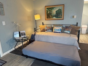 Ein Schlafzimmer mit Bett, Kissen, Schreibtisch, Lampe, einem gerahmten Gemälde und einem Schild an der Wand.