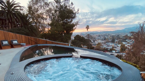 A hot tub with a curved brick design, surrounded by a wooden deck and lounge chairs.