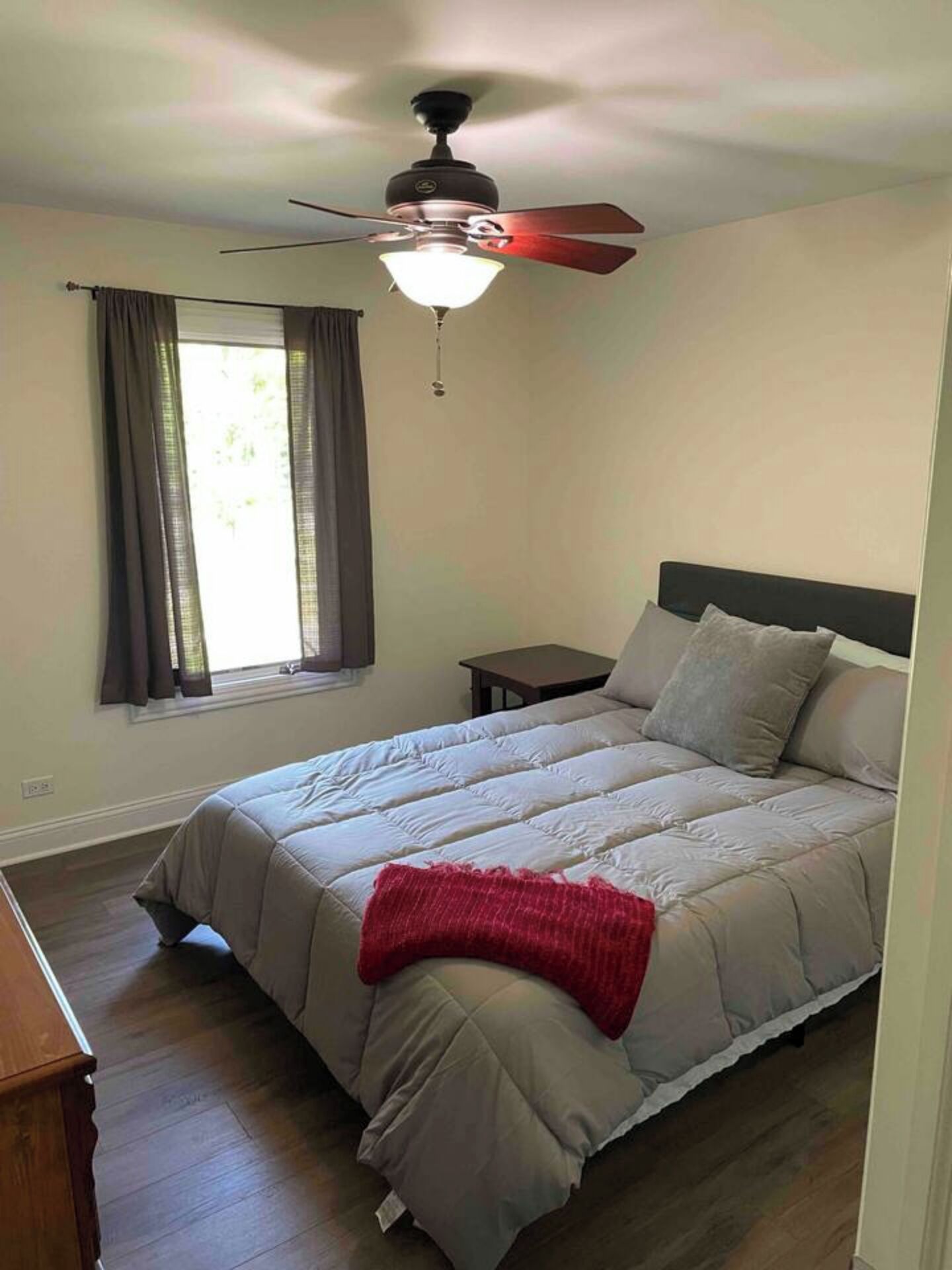 A bedroom with a bed, a ceiling fan, a window with curtains, and a nightstand.