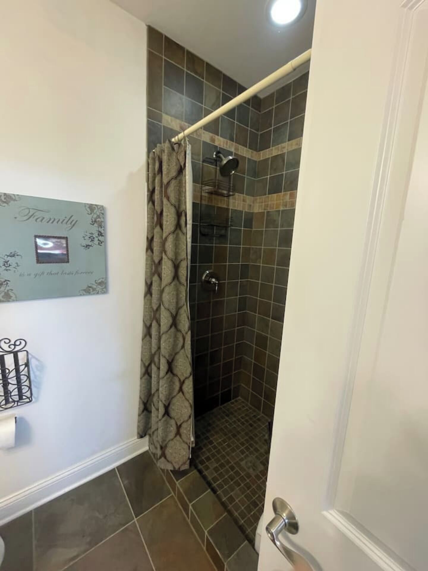 A bathroom with a shower, tiled walls, a curtain, a towel rack, and a framed sign on the wall.