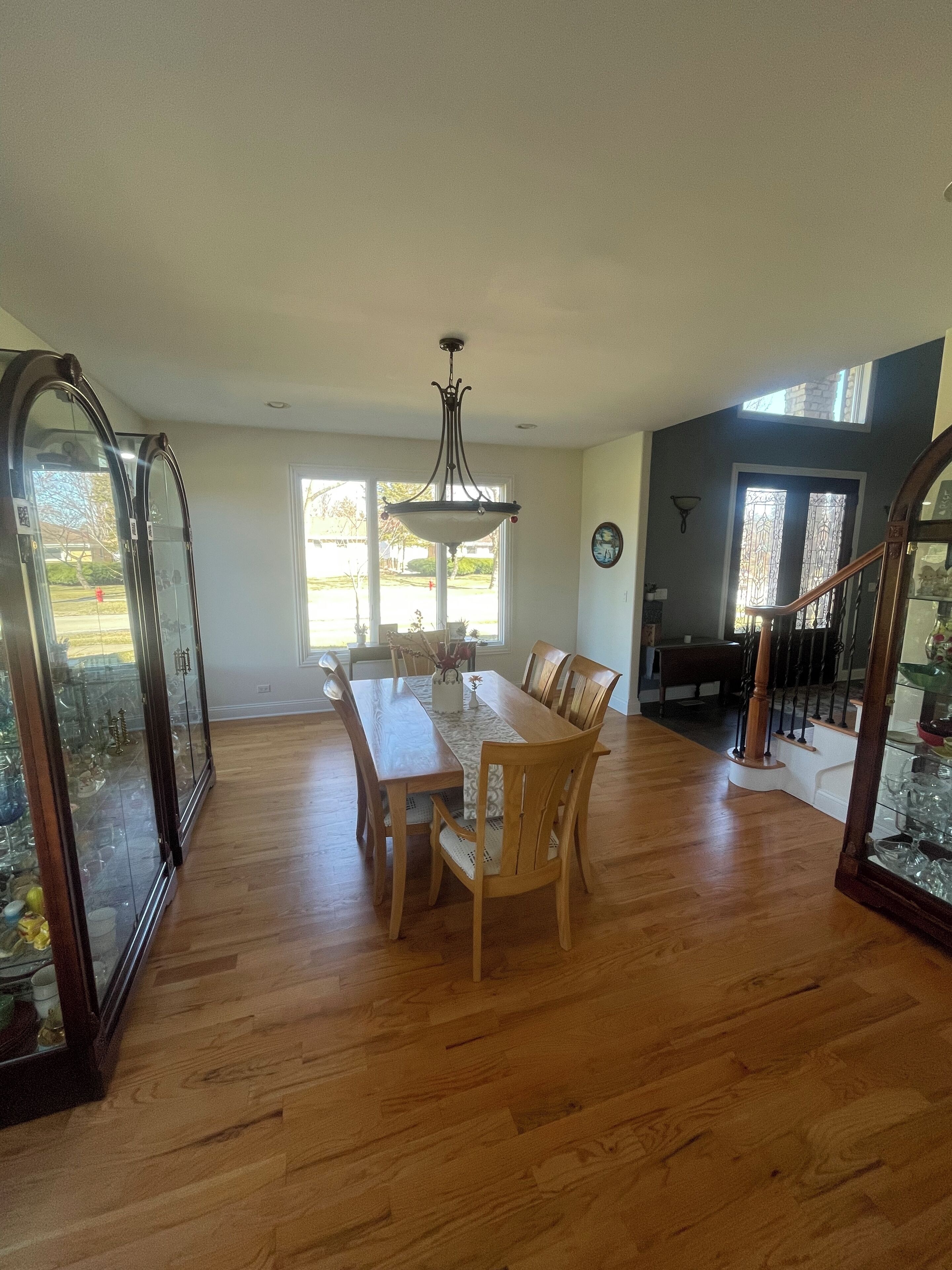 Un comedor amplio con mesa y sillas de madera, un candelabro y vistas al exterior a través de grandes ventanales.