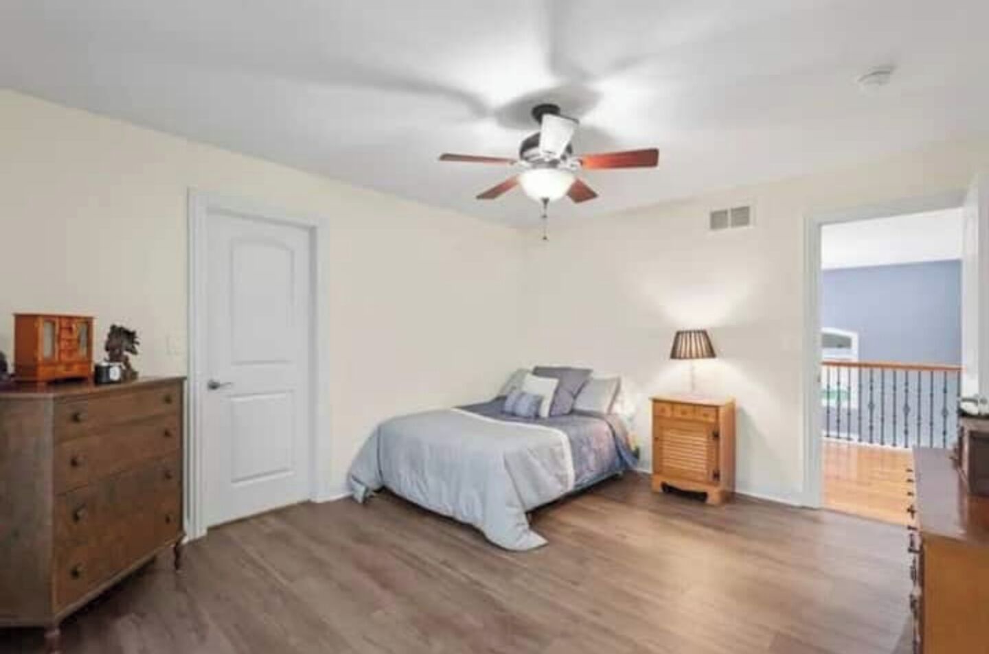 Ein Schlafzimmer mit Bett, Schminktisch, Nachttisch, Deckenventilator und einem Balkon.