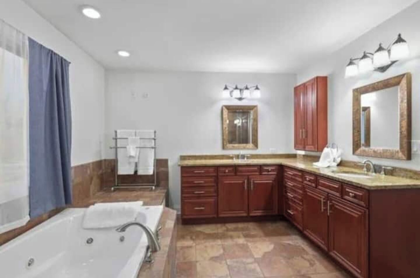 Un bagno moderno con una vasca da bagno ampia, un mobile vanitario con lavandino e uno specchio. Sono presenti armadietti in legno e un portascopevoli.