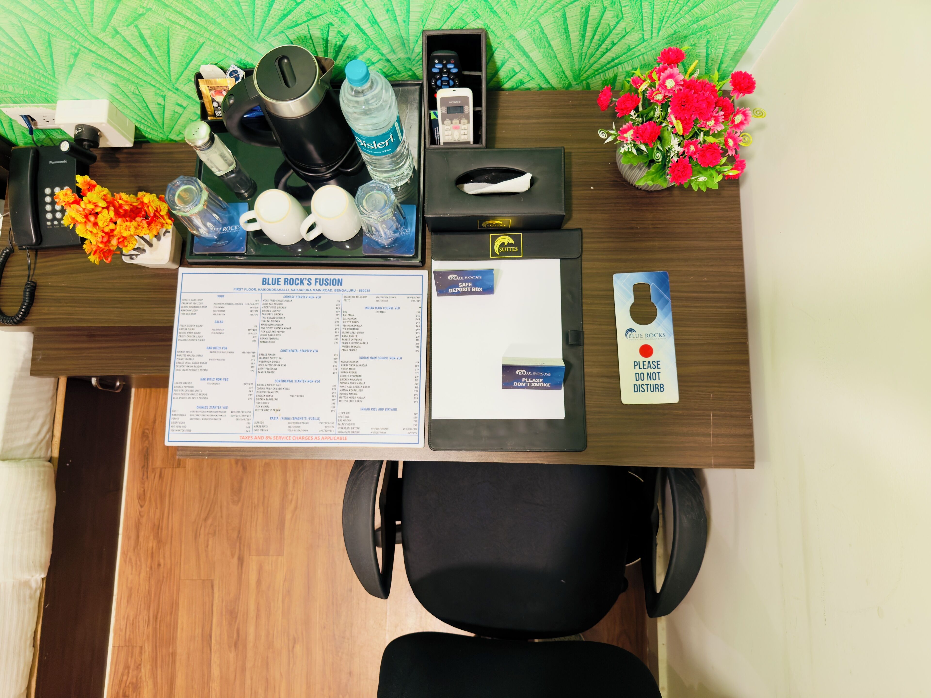 A hotel reception desk with a menu, a phone, a water bottle, a coffee maker, a remote control, a vase of flowers, and a "Please do not disturb" sign.