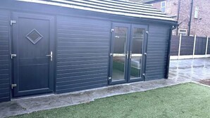 A dark-colored building with a metal roof, a door with a diamond-shaped window, and a glass door. - Newly Built Private Ensuite Room (Manchester)