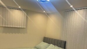 A single bed with a grey headboard and light green bedding in a room with beige walls and a ceiling light fixture. - Newly Built Private Ensuite Room (Manchester)